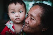 LAOS, 4000 ÎLES : Joli gosse dans les bras d'une femme âgée regardant la caméra . — Photo de stock