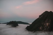 Nubes gruesas flotando en los picos de las altas montañas al atardecer - foto de stock