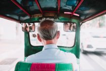 Back view of unrecognizable senior man driving rickshaw on city street. — Stock Photo