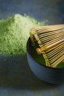 Crop bamboo whisk on bowl by pile of matcha — Stock Photo