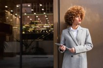 Mulher elegante em casaco cinza de pé com tablet digital na rua e olhando para longe . — Fotografia de Stock