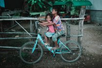 LAOS, 4000 ISLAS ÁREA: Niño y niña en bicicleta azul cerca de la valla en la calle del pueblo . - foto de stock