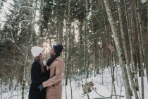 Romántica pareja multirracial abrazándose en el bosque de invierno - foto de stock