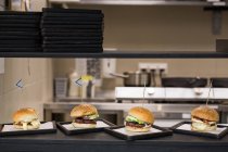 Savoureux hamburgers appétissants servis sur des assiettes sur la cuisine du restaurant . — Photo de stock
