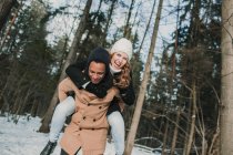 Hombre alegre llevando novia de vuelta en el bosque de invierno . - foto de stock