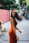 Веселая женщина в красном платье ходит по улице и смотрит через плечо в камеру — стоковое фото