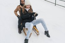 Glückliches Paar fährt Schlitten auf schneebedecktem Hügel und hat Spaß. — Stockfoto