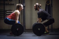 Vista lateral del hombre y la mujer haciendo ejercicio con barras en el gimnasio - foto de stock