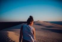 Вид сзади женщины, стоящей на песчаных дюнах и смотрящей в сторону
. — стоковое фото