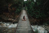 Mujer morena sentada en puente de cuerda en los trópicos - foto de stock