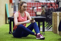 Frau sitzt im Fitnessstudio auf dem Boden und surft mit Smartphone — Stockfoto