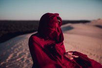 Неузнаваемая женщина, завернутая в красную ткань, стоящая на песчаных дюнах — стоковое фото