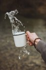 Recadrage main éclaboussant l'eau de tasse en métal dans la nature . — Photo de stock