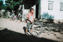 Nong khiaw, laos: Junge hält Stock und Rad in der Hand und schaut auf Dorfstraße weg. — Stockfoto