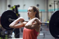Jovem mulher apto a se exercitar com barbell enquanto exercitando no ginásio . — Fotografia de Stock