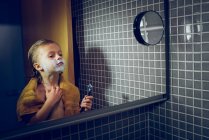 Уверенный маленький мальчик стоит перед зеркалом в ванной и бреется . — стоковое фото