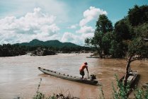 Unrecognizable man driving wooden canoe on dirty river in tropical countryside. — Stock Photo