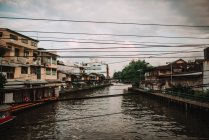 Perspective view to channel with dirty water and electric wires in cloudy day. — Stock Photo
