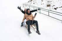 Pareja feliz montando trineo en la colina nevada - foto de stock