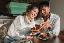 Веселая пара смотрит смартфон в кафе — стоковое фото