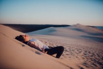 Mujer morena tumbada en la arena y disfrutando del sol . - foto de stock