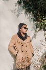 Uomo riflessivo in occhiali da sole alla moda e cappotto appoggiato alla parete — Foto stock
