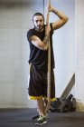 Sportlicher Mann hält Seil in Turnhalle und blickt in Kamera — Stockfoto