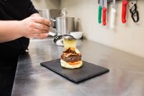 Couper les mains du cuisinier en mettant de la sauce sur le hamburger — Photo de stock