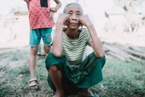НОНГ-ХИЯУ, ЛАОС: Пожилая местная женщина сидит на траве и смотрит в камеру — стоковое фото