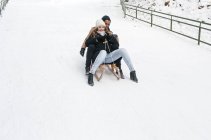Счастливая пара катается на санях на снежном холме — стоковое фото