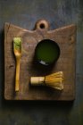 Matcha tea in scoop by bamboo whisk with cup on cutting board — Stock Photo