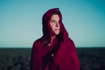 Portrait femme enveloppé dans du tissu rouge debout sur le sable et regardant loin — Photo de stock