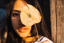 Молодая женщина держит сухой лист перед лицом и смотрит в камеру — стоковое фото