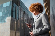Вид сбоку на стильную женщину, стоящую на улице и просматривающую смартфон — стоковое фото