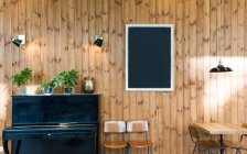 Tableau noir vide suspendu au mur en bois dans la chambre avec piano et chaises . — Photo de stock