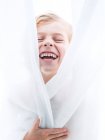 Jovem alegre envolto em cortinas e rindo — Fotografia de Stock