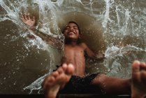 LAOS, 4000 ISOLE AREA: Ragazzo senza maglietta in pantaloncini che ride cadendo nell'acqua del fiume sporco . — Foto stock