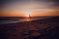 Silhouette of woman jumping in midair on sand beach at sunset — Stock Photo