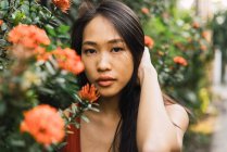Sensual jovem mulher posando no arbusto florescendo laranja e segurando o cabelo — Fotografia de Stock