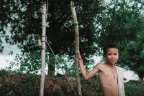 LAOS, 4000 ISOLE AREA: Ragazzo senza maglietta in piedi in natura vicino a due pali di legno e sorridente
. — Foto stock