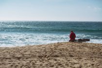 Visão traseira da mulher sentada na costa do mar no dia ensolarado — Fotografia de Stock