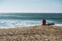 Vue arrière de la femme assise sur le bord de la mer par une journée ensoleillée — Photo de stock