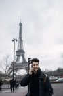 Lächelnder junger Mann spricht auf Smartphone im Hintergrund des Eiffelturms. — Stockfoto