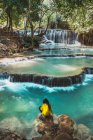 Вид сзади на сидящего туриста у тропического водопада — стоковое фото