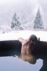 Вид на спину жінки, що плаває на вулиці, пориньте у ванну в зимовій природі . — стокове фото