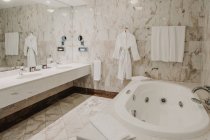 Vista interior del baño de lujo con espejo grande y albornoz blanco . - foto de stock
