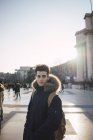 Pensive young man standing on city square in sun flare and looking away. — Stock Photo