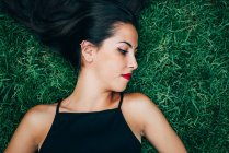 Брюнетка с красными губами, лежащая в траве — стоковое фото