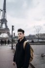 Молодой человек с рюкзаком стоит на фоне Эйфелевой башни . — стоковое фото
