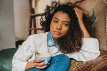 Frau sitzt mit Tasse Kaffee auf Sofa und blickt in Kamera — Stockfoto